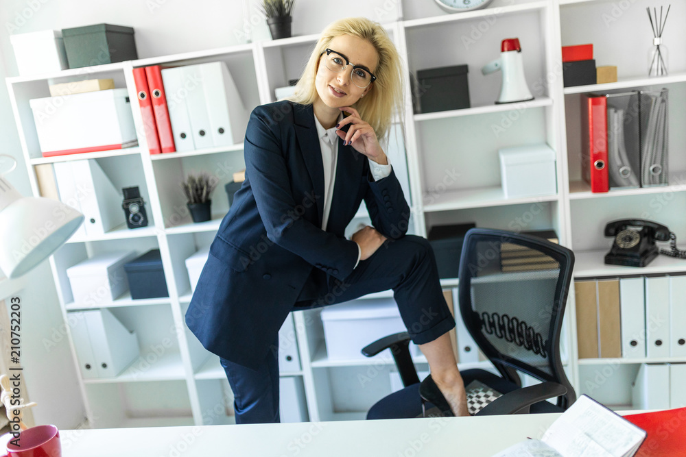 A young girl stands near a table in the office, putting her foot on a chair. A young girl stands near a table in the office, putting her foot on a chair.