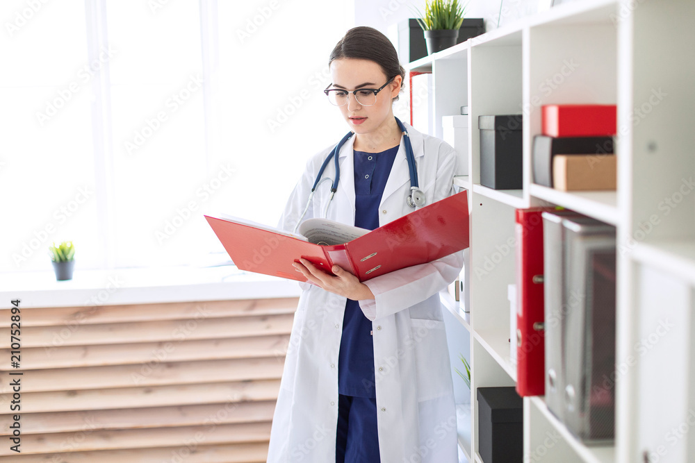 A beautiful young girl in a white robe is standing near the shelter and flips through a red folder with documents.