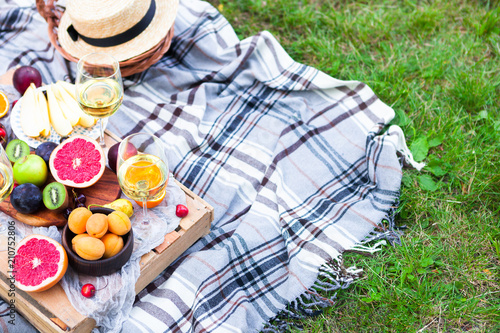 Picnic background with white wine and summer fruits on green grass, top view