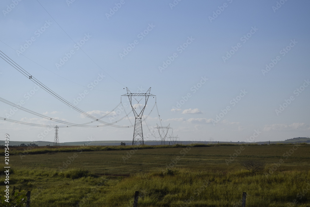 Torre de distribuição elétrica através de campo verde, céu azul	