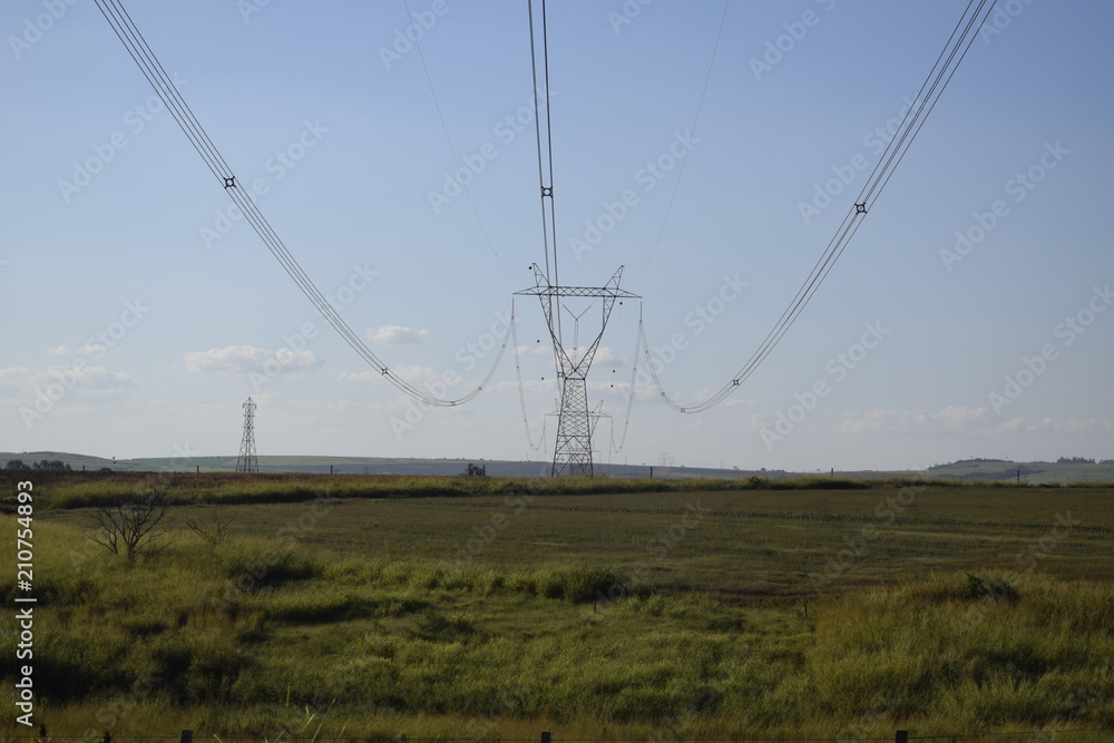 Torre de distribuição elétrica através de campo verde, céu azul