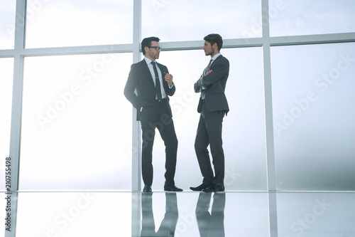 two businessmen standing near a large office window