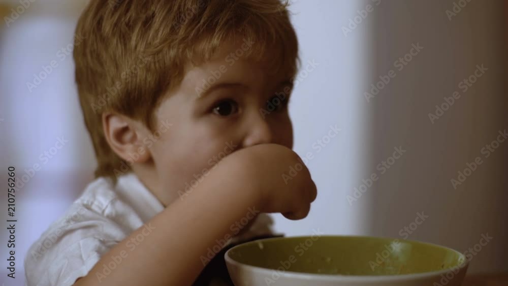 Kid eating bowl of oatmeal for breakfast. Child eating while watch cartoons Kid eating bowl of oatmeal for breakfast. Child eating while watch cartoons