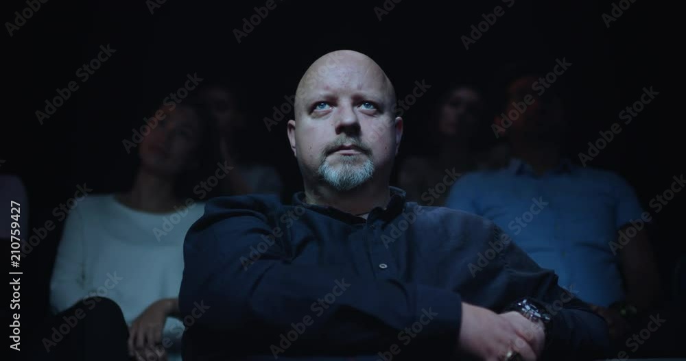 Slow crane up shot of a bald middle aged man siting in a movie theatre. Slow crane up shot of a bald middle aged man siting in a movie theatre.