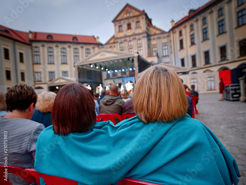A warm plaid helps women not to get frozen in the evening at a concert outdoors. Women are covered with a blanket to warm up during the performance in cold weather. © Tricky Shark