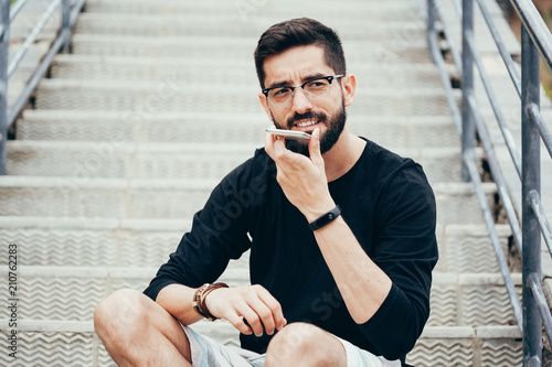 Leisure, technology, communication and people concept - young man using voice command recorder or calling on smartphone at street