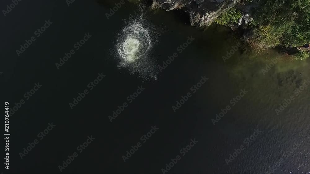 Overhead aerial, man jumps off cliff into lake Overhead aerial, man jumps off cliff into lake