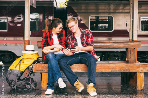 Happy young couple travellers together on vacation use phone at the train station, travel concept, couple concept
