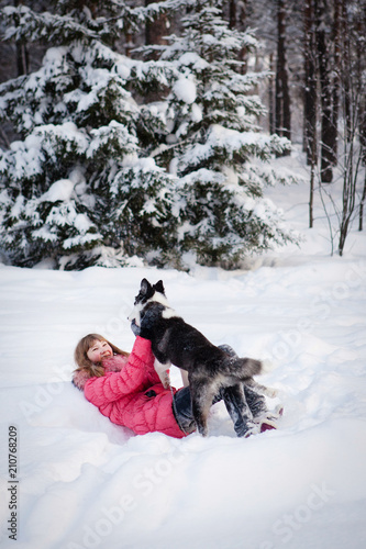 Young beautiful girl playing with siberian husky dog in the winter park