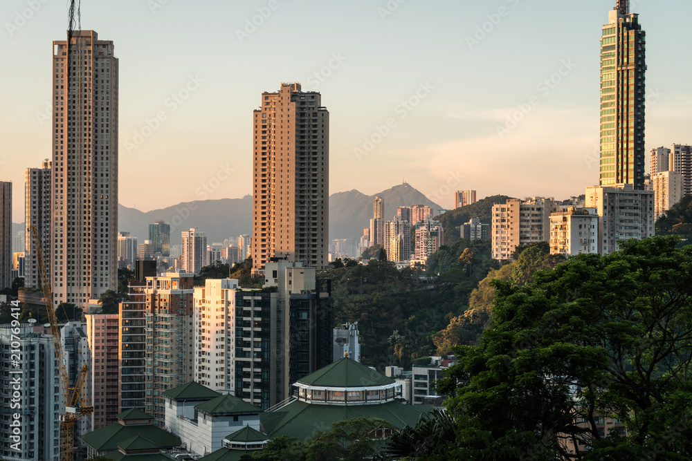 Obraz premium Sunset over tall apartment tower in Happy Valley in Hong Kong island with the peaks of kowloon in the back in Hong Kong, China