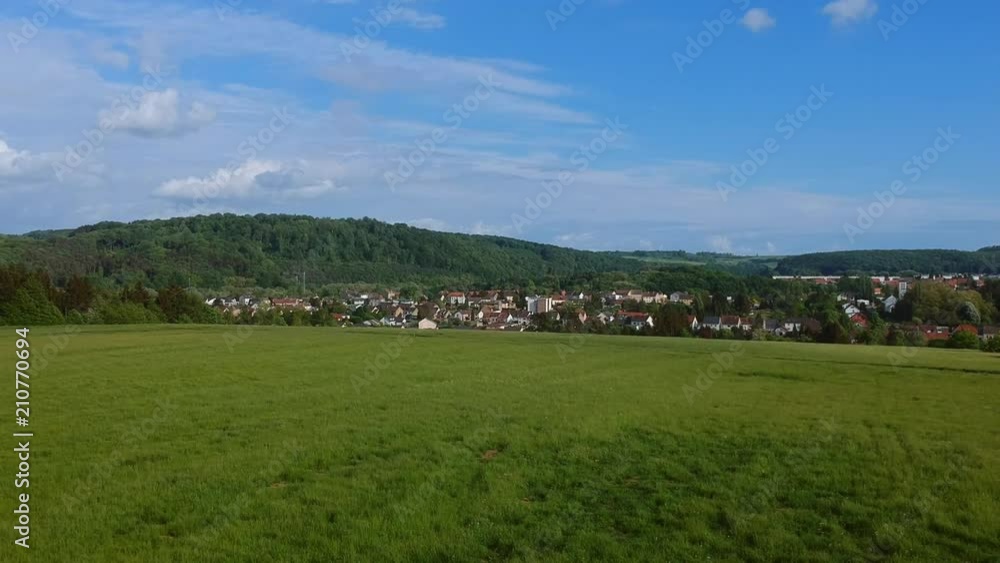 Wide angle view over a green field and a small village - aerial drone flight