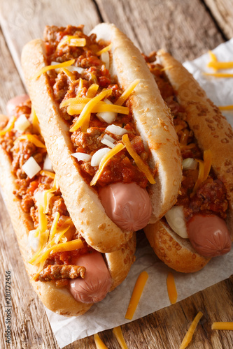 Chili hot dogs with cheese cheddar, spicy ground beef, onion and sauce close-up. vertical