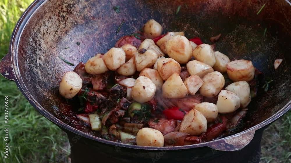 Cooking of pilaf. Grilled vegetables with chopped lamb in a cauldron, outdoor. stewed food. camping concept Cooking of pilaf. Grilled vegetables with chopped lamb in a cauldron, outdoor. stewed food. camping concept