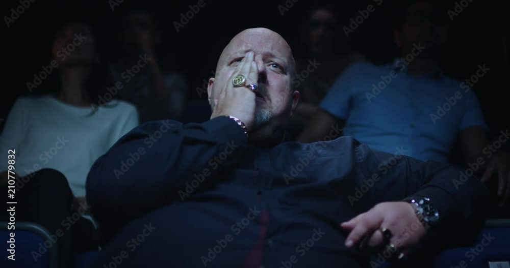 A man wipes away a tear while watching a sad movie at the movie theatre.