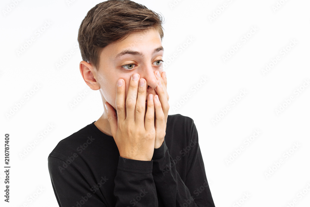 Photo emotional teenager, guy in black t-shirt, shows the emotions of fear, closing his mouth with his hands, on a white background, for advertising text insertion Photo emotional teenager, guy in black t-shirt, shows the emotions of fear, closing his mouth with his hands, on a white background, for advertising text insertion