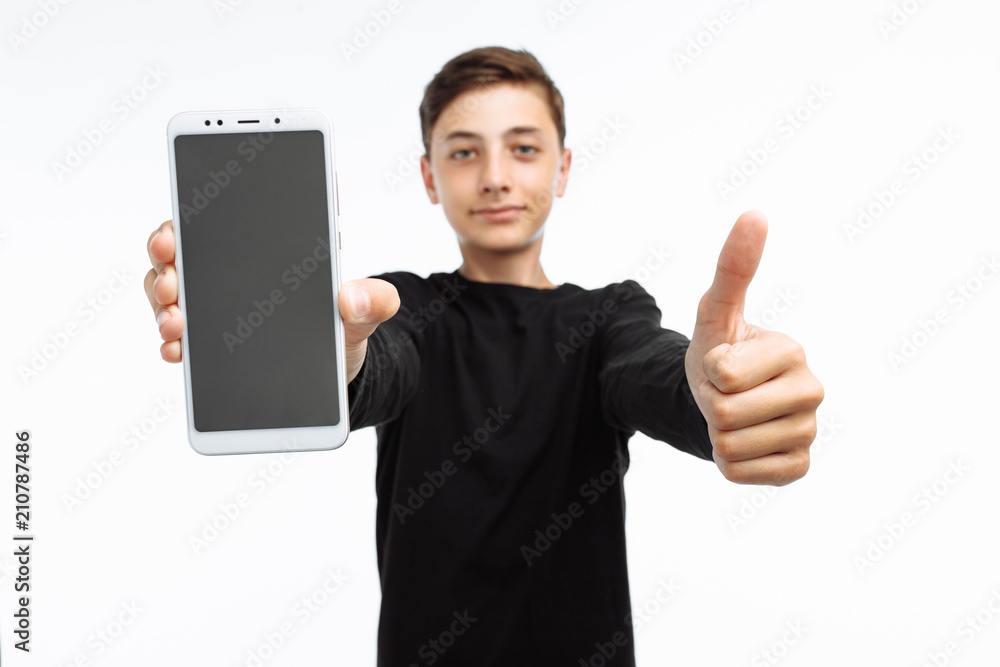 Portrait of a teenager, a guy holding a phone with a white screen, and shows a finger class, in a black t-shirt, on a white background, advertising, text insert Portrait of a teenager, a guy holding a phone with a white screen, and shows a finger class, in a black t-shirt, on a white background, advertising, text insert