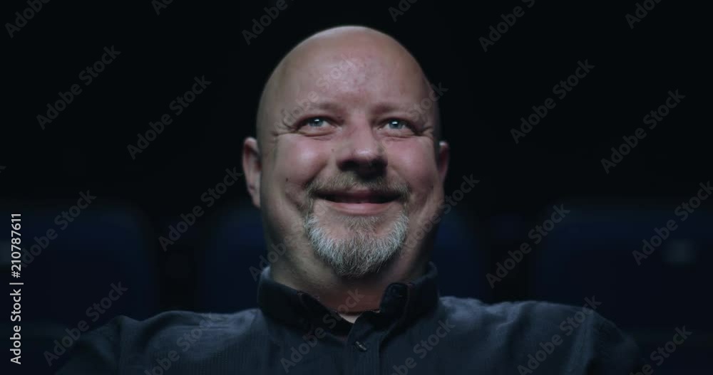 Bald man at the movie theatre beings to smile. Bald man at the movie theatre beings to smile.