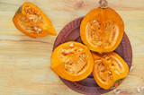 Raw pumpkin slices with seeds on the brown plate on the wooden background. Ingredients for tasty autumn soup. Top view
