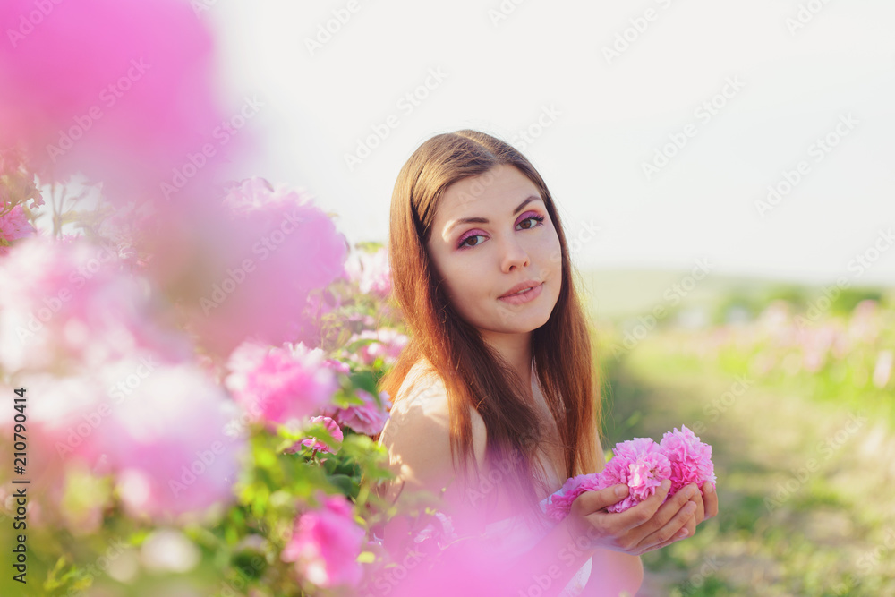 Fototapeta premium Beautiful young woman posing near roses in a garden.