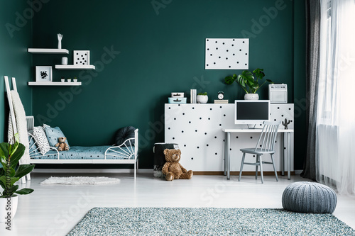 Cozy bedroom interior with teddy bears, single bed, desk and computer, dotted wall and pouf on the carpet. Place your product photo