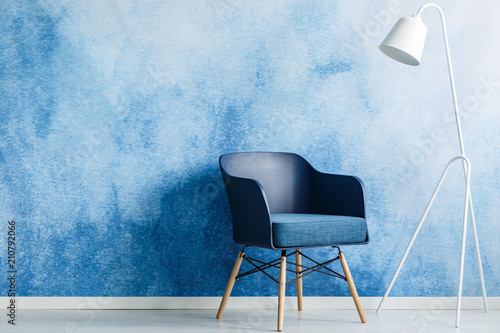 Modern dark blue chair and white metal lamp against ombre wall in a minimal style waiting room interior. Copy space. Real photo.