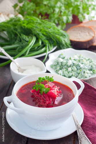 Vegetarian borsch with fresh herbs in a white serving plate, selective focus