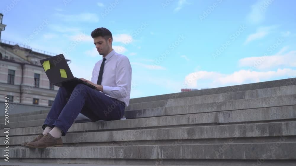 young successful guy student working on the street on laptop. A man in a white shirt and tie. nice young man working on a project 4K young successful guy student working on the street on laptop. A man in a white shirt and tie. nice young man working on a project 4K