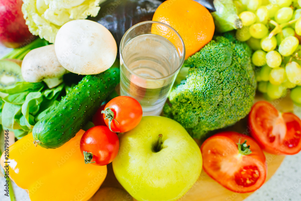 Many different fruits and vegetables with glass of water in the middle
