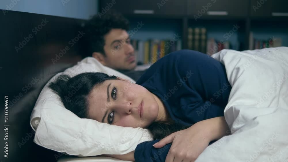 couple in crisis: sad depressed woman in bed with her husband pretend to sleep couple in crisis: sad depressed woman in bed with her husband pretend to sleep