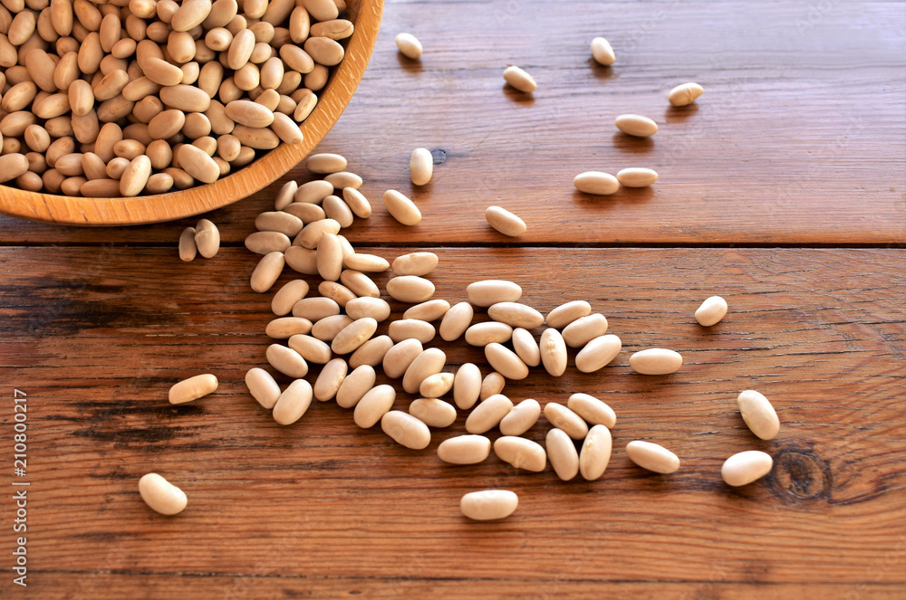 White beans dry, uncooked beans in a bowl, scattered on a table. White beans dry, uncooked beans in a bowl, scattered on a table.