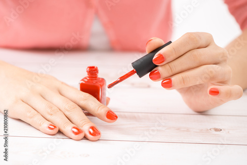 Female hands with red manicure and an open bottle of varnish on the table