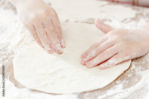 Child hands prepares the dough with flour for bread or pizza. Bakery background.