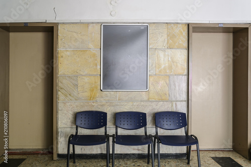 blackboard on a old hospital wall surrounding by doors a chairs.