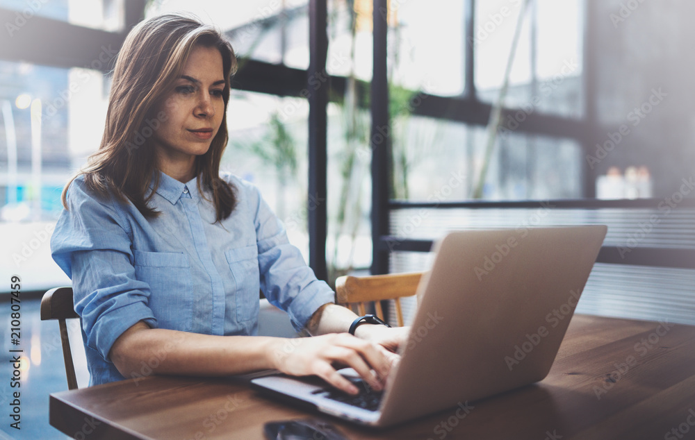Young pretty girl working on laptop and using mobile smartphone at her workplace at modern office center.Horizontal.Blurred background. Young pretty girl working on laptop and using mobile smartphone at her workplace at modern office center.Horizontal.Blurred background.