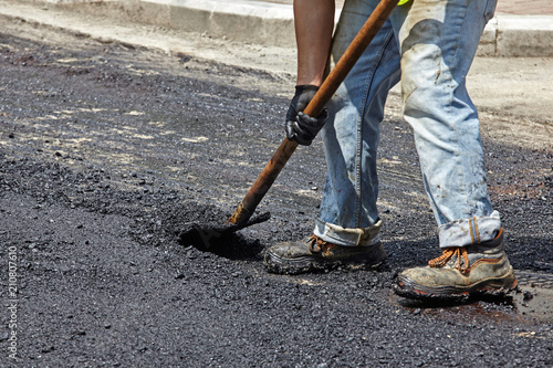 Worker using asphalt paver tool during road construction.