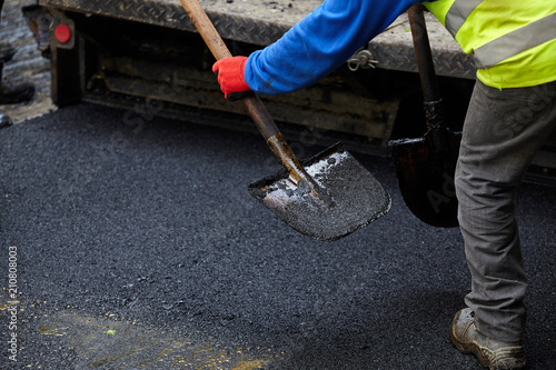 Worker operating asphalt paver machine during road construction.