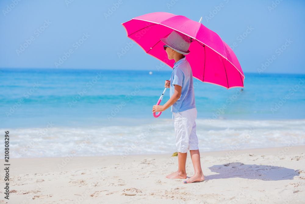 Boy with a pink umbrella on the sandy beach