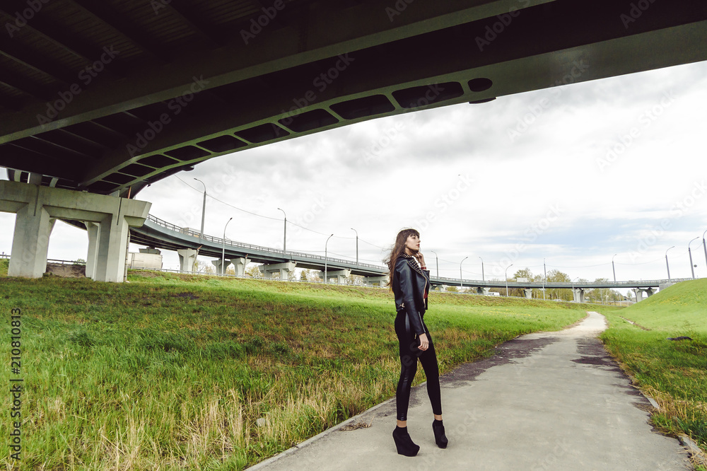 young beautiful stylish woman in fashionable black clothes, a burgundy cardigan and a dark leather jacket posing outdoors near the main road junction