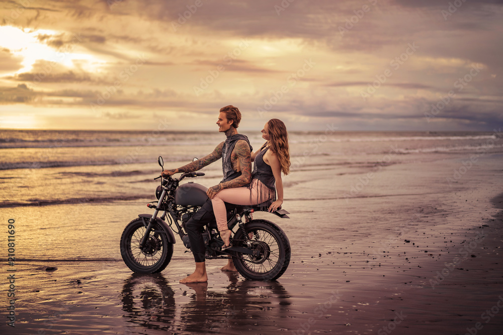 tattooed boyfriend and girlfriend sitting on motorcycle at beach during sunrise tattooed boyfriend and girlfriend sitting on motorcycle at beach during sunrise