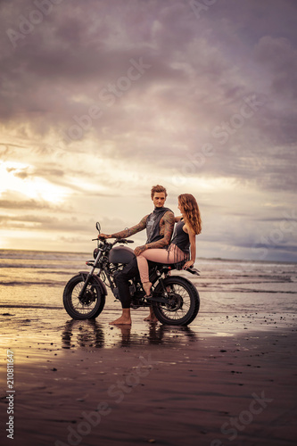 boyfriend and girlfriend sitting on motorcycle at sandy beach