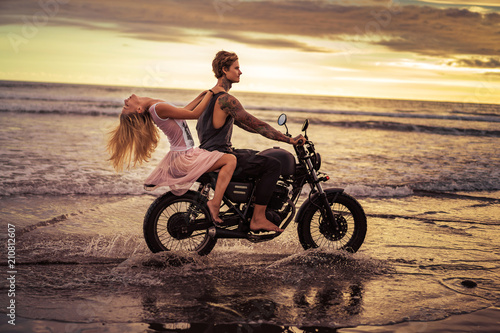 attractive couple riding motorcycle on ocean beach during sunrise