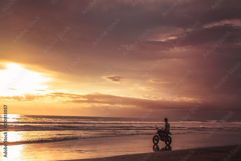 man sitting on motorbike on seashore and looking at beautiful sunset man sitting on motorbike on seashore and looking at beautiful sunset