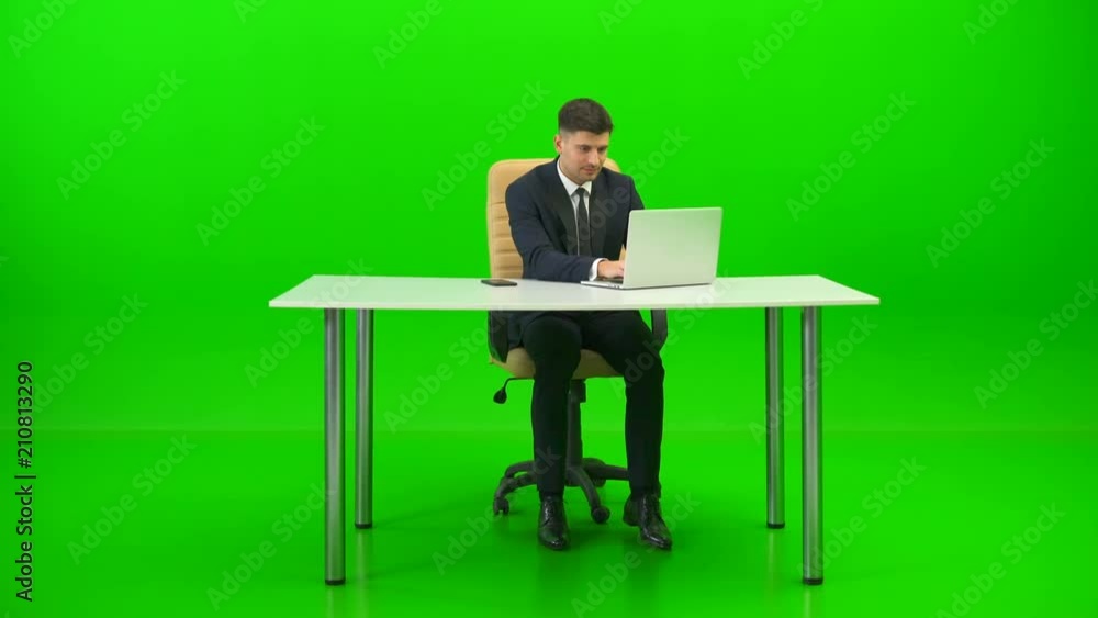 The businessman works at the desktop and phones on the green background The businessman works at the desktop and phones on the green background