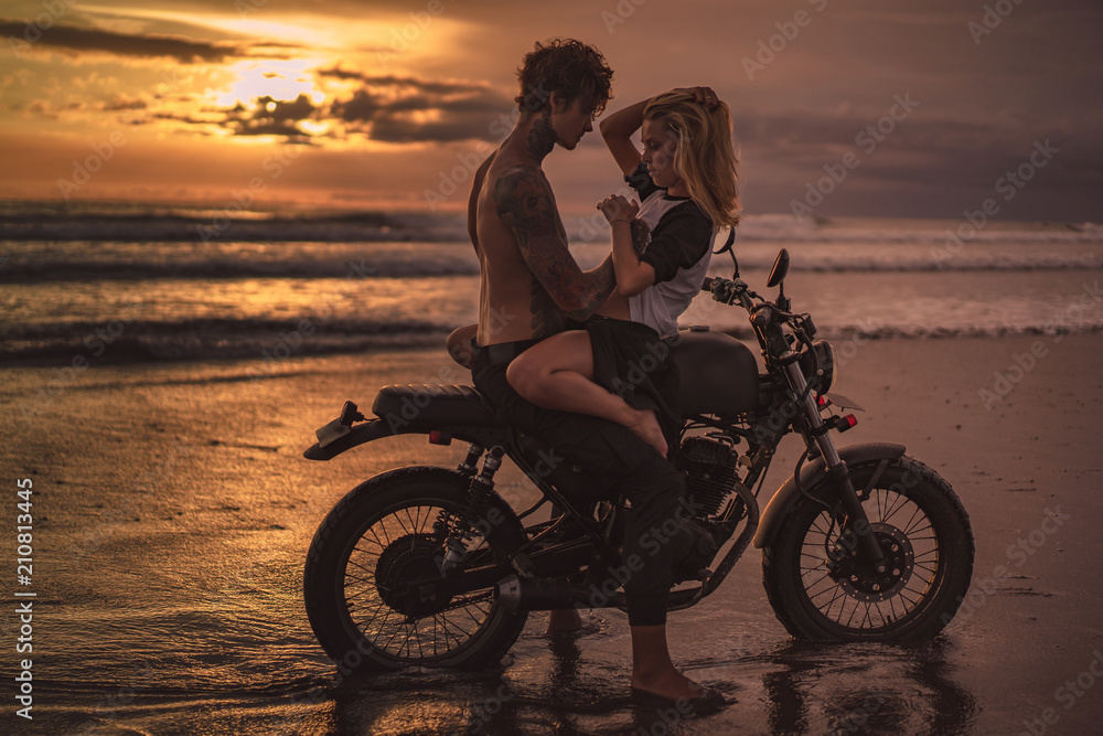 Fototapeta sexy girlfriend and boyfriend cuddling on motorbike at beach during sunset