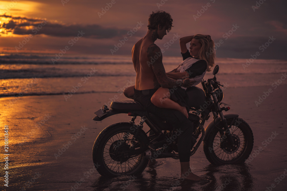 Fototapeta seductive couple cuddling on motorbike at beach during sunset