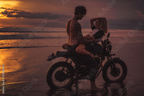 seductive couple cuddling on motorbike at beach during sunset