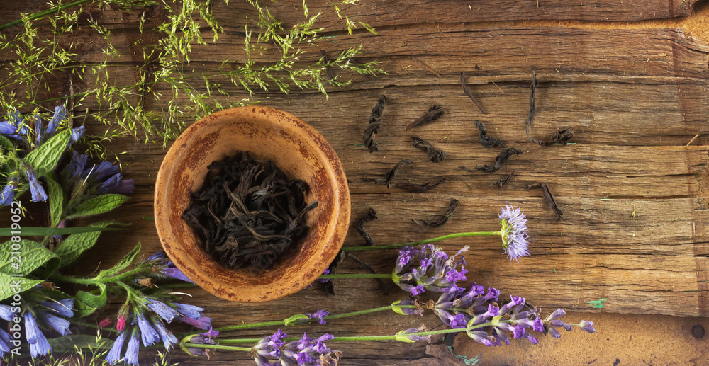 Petals of black tea in a small clay bowl, around the flowers of the field and twigs of lavana. Daylight. Top View Petals of black tea in a small clay bowl, around the flowers of the field and twigs of lavana. Daylight. Top View
