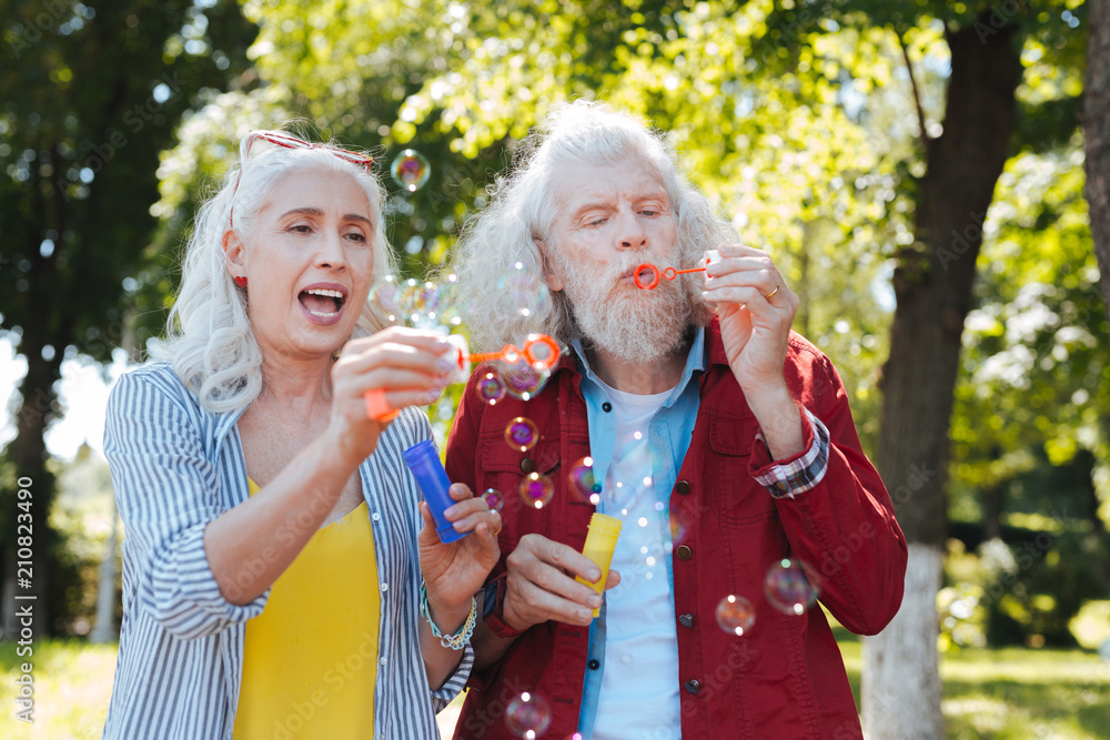Fototapeta premium Interesting activity. Nice happy couple standing together while blowing soap bubbles