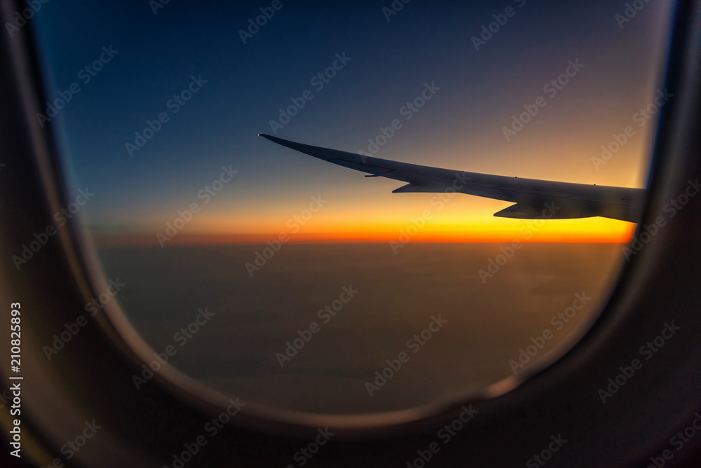 Naklejka premium Skrzydło sylwetki samolotu w widoku wschód słońca przez okno.