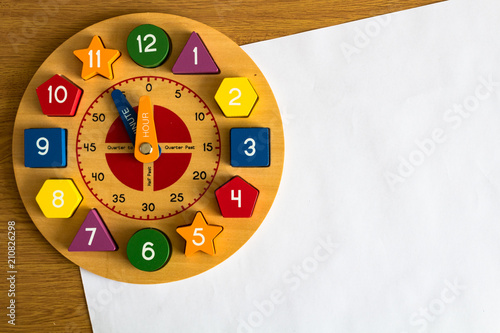 Toy wooden clock on a sheet of white paper, on a wooden background
